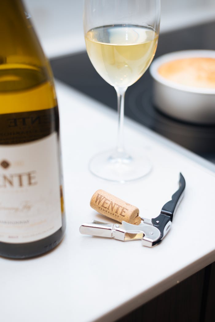 A glass of white wine beside a bottle and corkscrew on a table, ideal for wine lovers.